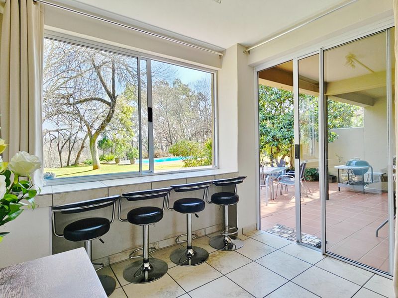 Enclosed patio area featuring tiled flooring, a built-in breakfast bar, and large sliding glass doors providing access to the outdoor garden and pool area.