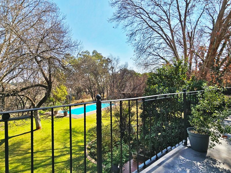 A spacious balcony featuring a wrought iron railing, overlooking a lush garden and a private swimming pool.