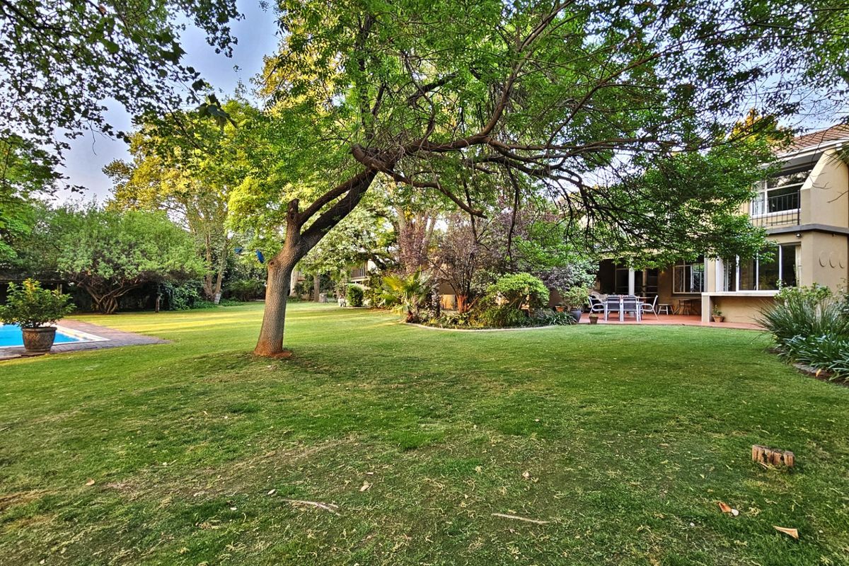 Spacious rear garden featuring a well-maintained lawn, mature trees, a swimming pool, and a paved patio area attached to the townhouse.