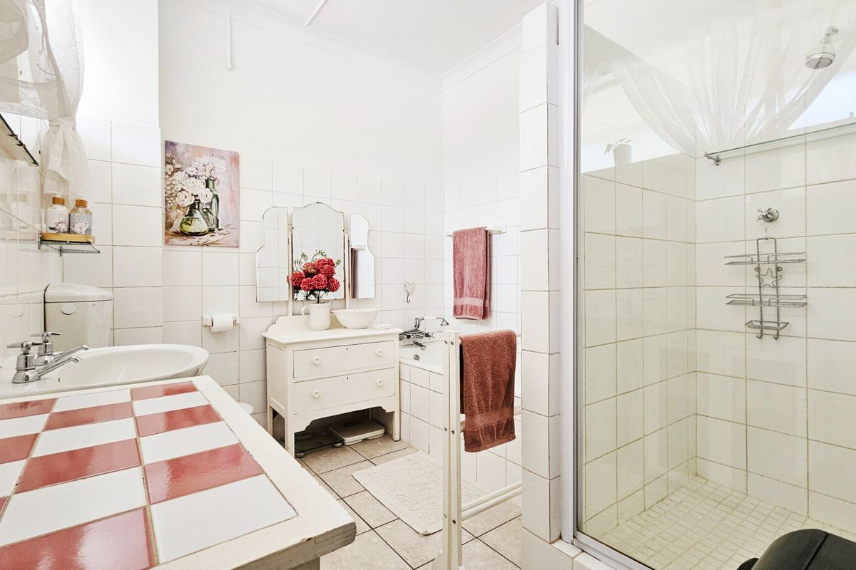 A functional bathroom featuring a tiled shower enclosure, built-in bathtub, and a vanity area with tiled countertop, offering a classic layout.
