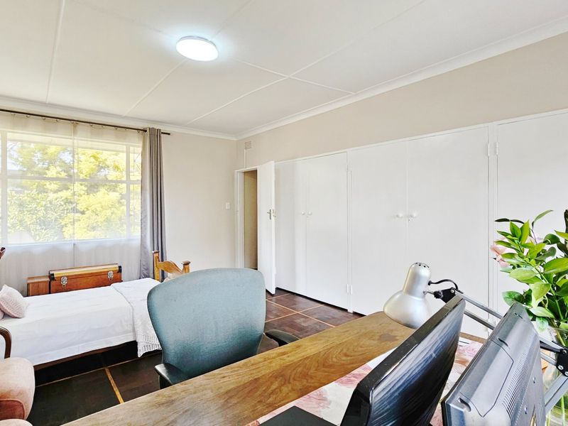 A functional bedroom featuring built-in cupboards, tiled flooring, and a large window that provides ample natural light.