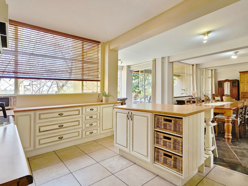 Spacious open-plan kitchen and dining area featuring classic cabinetry, timber countertops, tiled flooring, and large windows providing natural light and garden views.