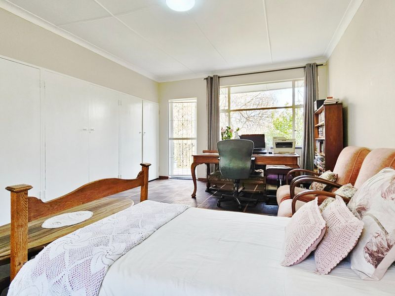 Spacious bedroom featuring built-in cupboards, tiled flooring, and a large window providing natural light and access to a security gate.