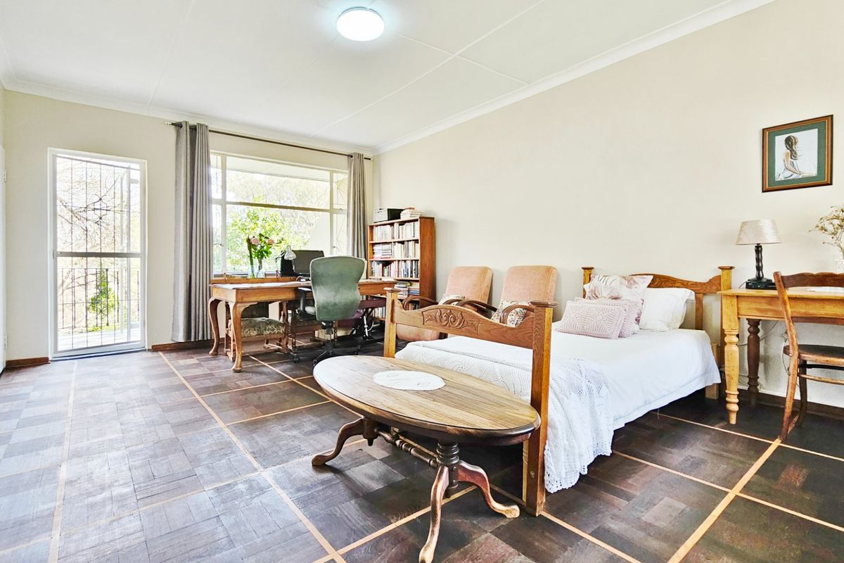 Spacious bedroom featuring classic parquet flooring, large windows for natural light, and direct access to an outdoor area via a security gate.