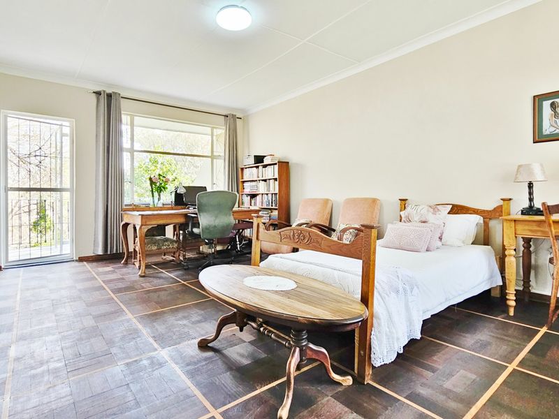 Spacious bedroom featuring classic parquet flooring, large windows for natural light, and direct access to an outdoor area via a security gate.