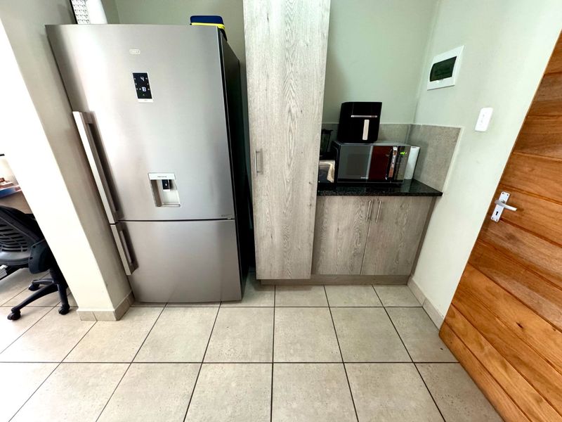 A compact scullery area featuring built-in cabinetry, stone countertops, and tiled flooring, providing functional storage and prep space adjacent to the main living area.