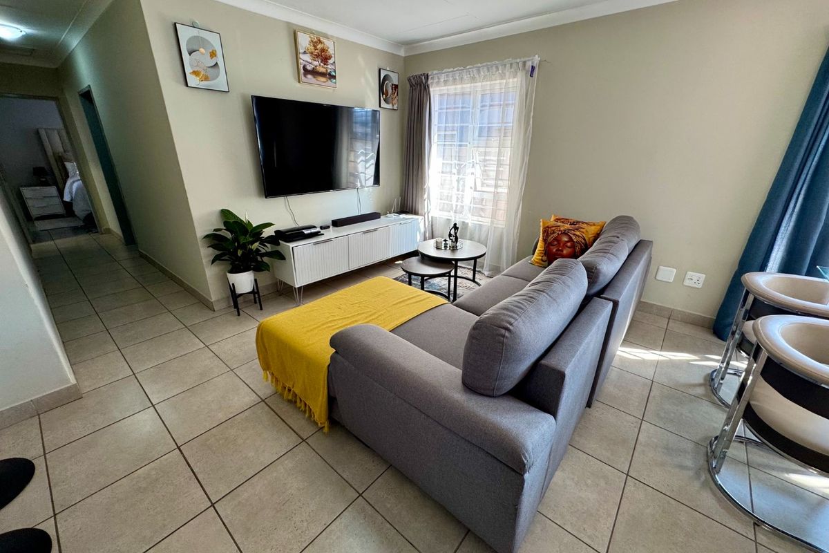A well-maintained living room featuring neutral tiled flooring, coved ceilings, and a functional layout with natural light from the window.