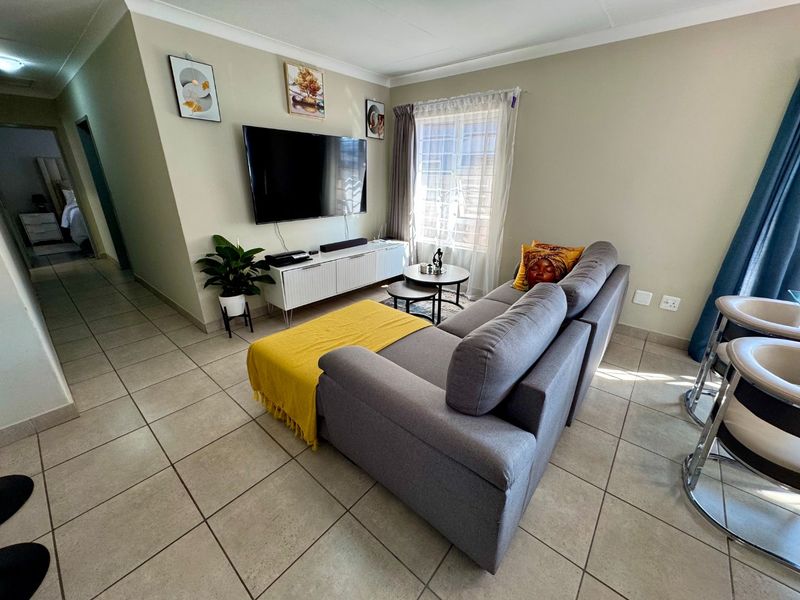 A well-maintained living room featuring neutral tiled flooring, coved ceilings, and a functional layout with natural light from the window.