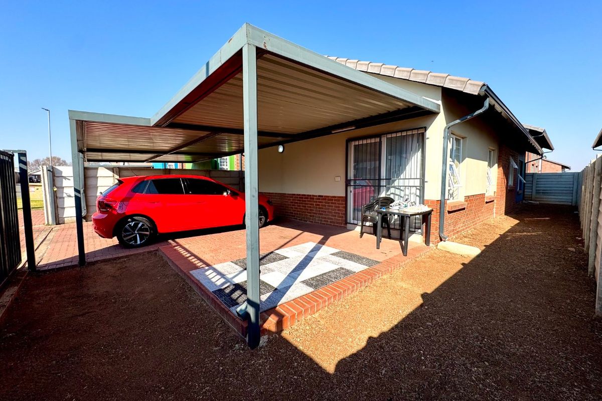 Rear exterior view of the townhouse featuring a covered carport, paved patio area, and brick facade with secure sliding door access.