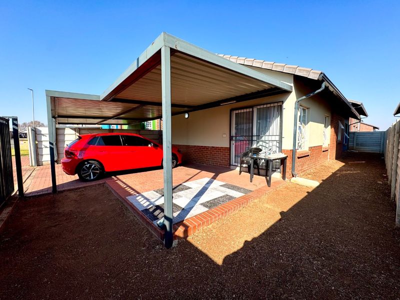 Rear exterior view of the townhouse featuring a covered carport, paved patio area, and brick facade with secure sliding door access.