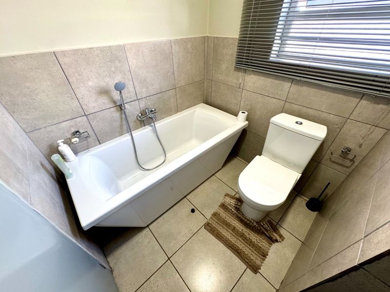 A functional bathroom featuring a bathtub with a handheld shower mixer, a toilet, and neutral-toned wall and floor tiling.