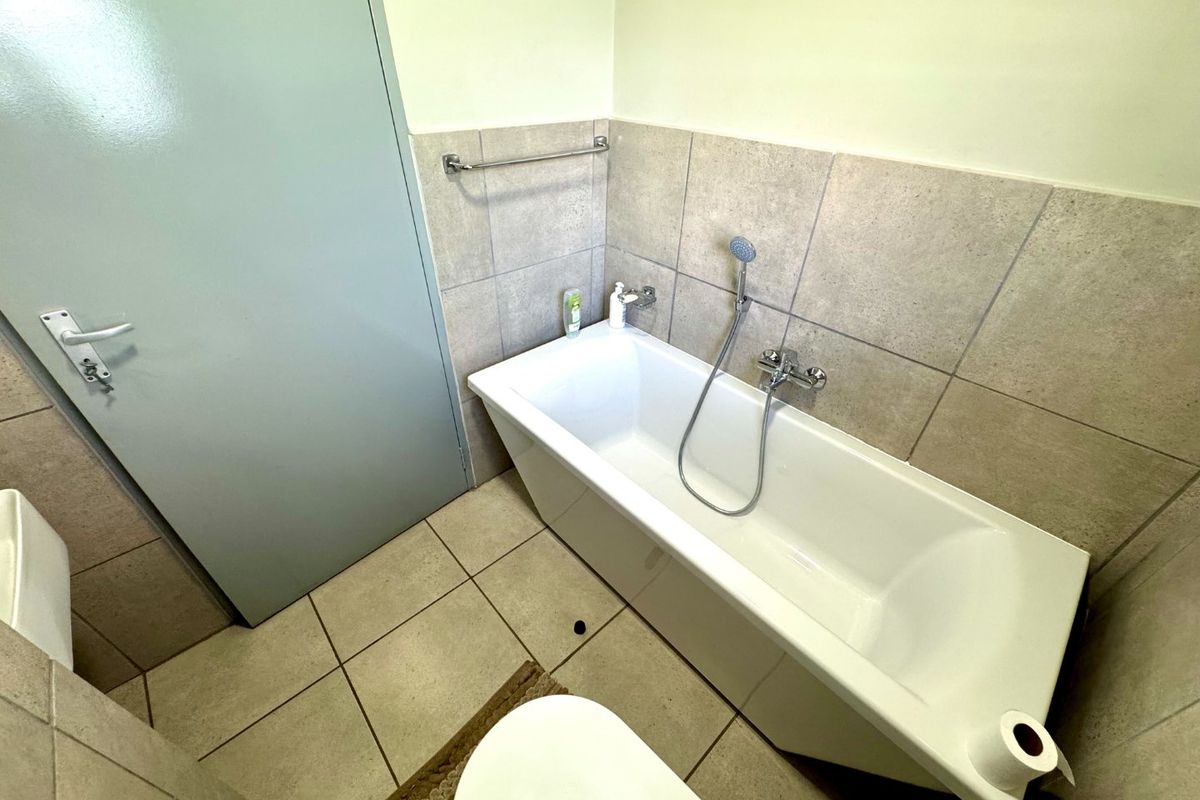 A functional bathroom featuring a bathtub with a handheld shower mixer, neutral wall and floor tiling, and a wall-mounted towel rail.