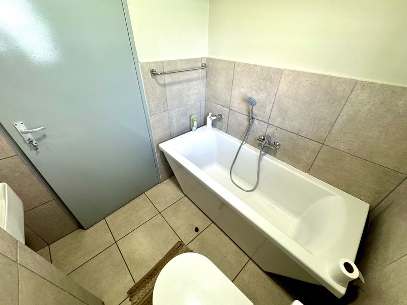 A functional bathroom featuring a bathtub with a handheld shower mixer, neutral wall and floor tiling, and a wall-mounted towel rail.