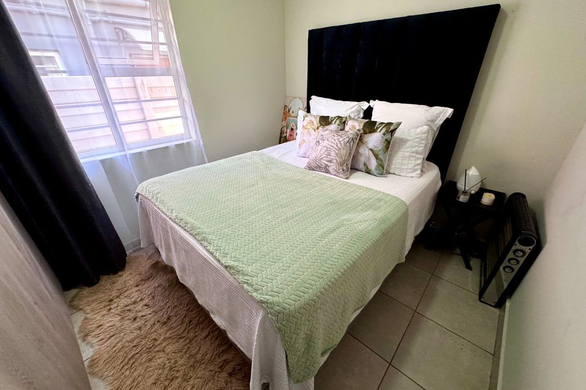 A compact bedroom featuring tiled flooring and a window fitted with security bars, providing a functional and well-lit sleeping space.