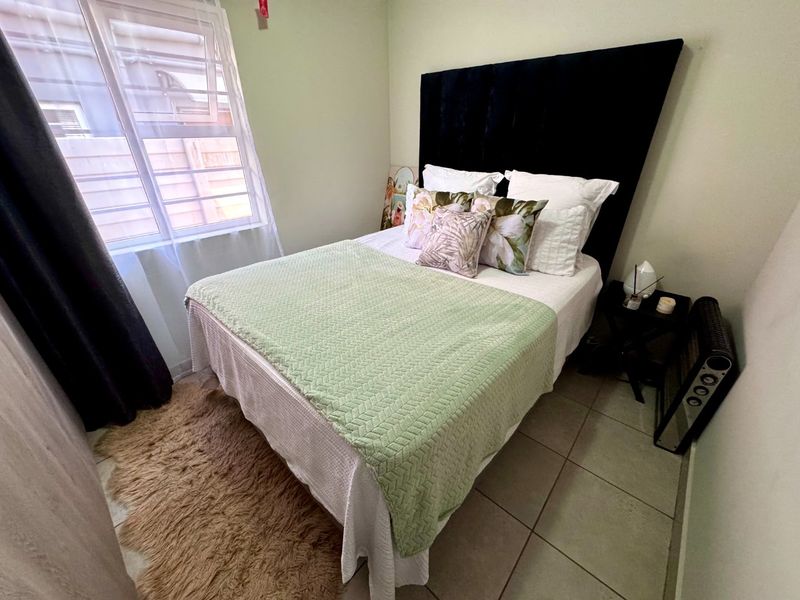 A compact bedroom featuring tiled flooring and a window fitted with security bars, providing a functional and well-lit sleeping space.
