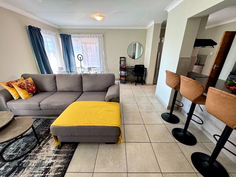 Open-plan living area featuring tiled flooring, coved cornicing, and a breakfast bar connecting to the kitchen space.