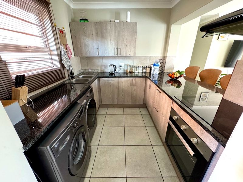 A functional kitchen featuring granite countertops, built-in cabinetry, integrated oven and hob, and tiled flooring with a breakfast bar area.