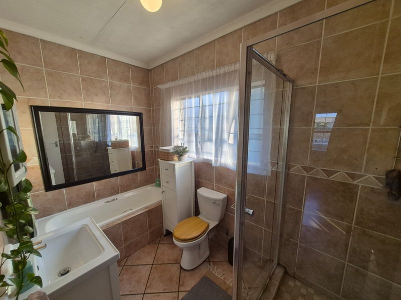 A functional bathroom featuring a built-in bathtub, separate shower enclosure, tiled walls and flooring, and a vanity basin.
