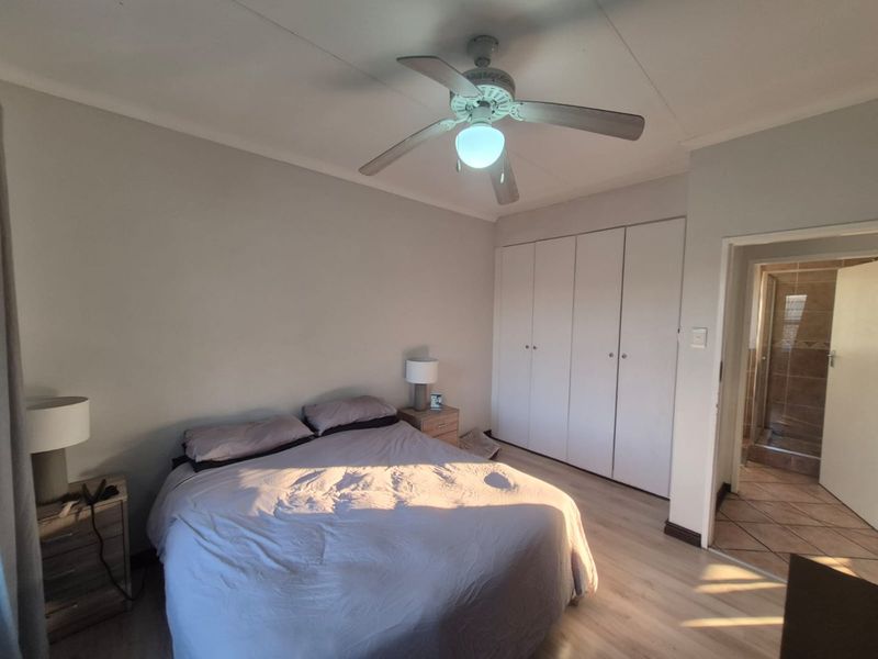 A well-lit bedroom featuring laminate flooring, a ceiling fan, and built-in cupboards, with direct access to an en-suite bathroom.