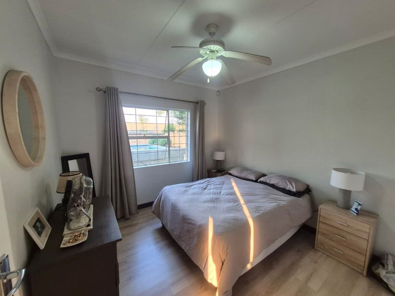 A well-maintained bedroom featuring laminate flooring, a ceiling fan, and a window with security bars overlooking the exterior pool area.