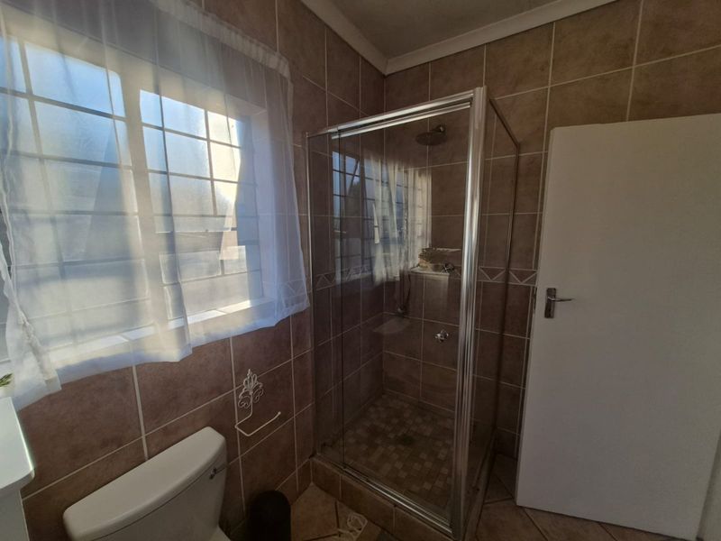 A functional bathroom featuring a glass-enclosed shower, tiled walls and flooring, and a window with security bars.