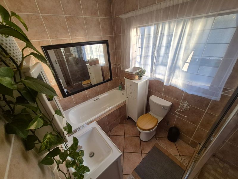 A functional bathroom featuring a built-in bathtub, toilet, and vanity basin with neutral ceramic tiling throughout.