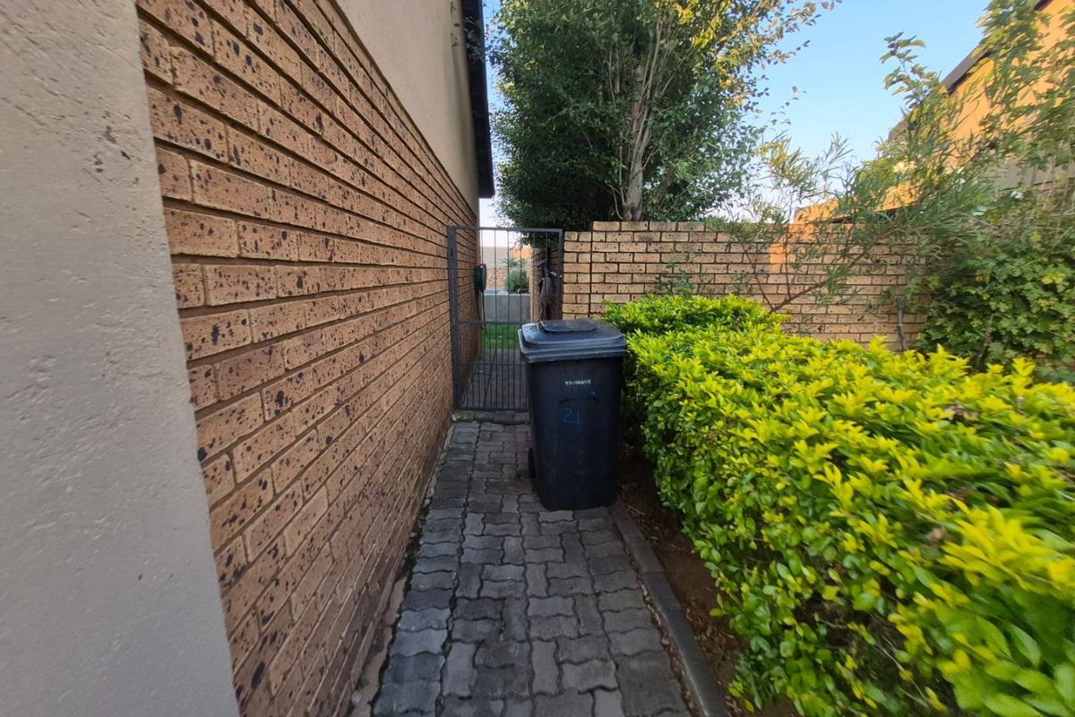 A side pathway featuring a paved walkway, brick boundary wall, and metal gate, providing access to the rear of the townhouse property.