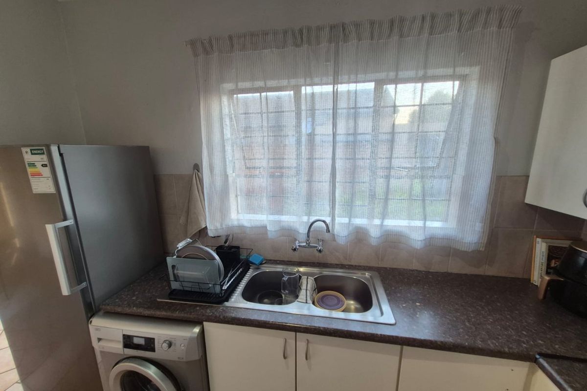 A functional kitchen area featuring a double bowl stainless steel sink, laminate countertops, tiled backsplash, and built-in cabinetry with space for appliances.
