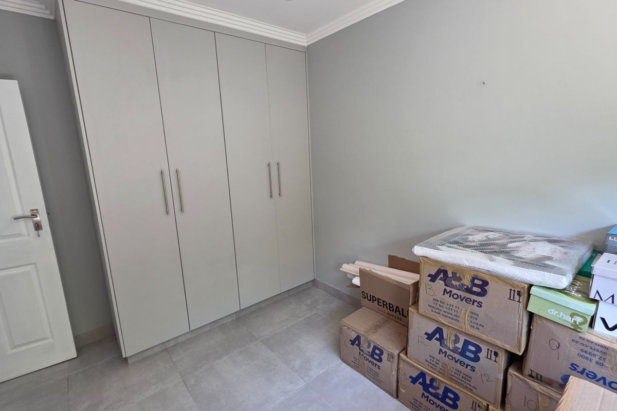 A clean bedroom featuring neutral-toned built-in cupboards, modern tiled flooring, and crisp white trim, offering a versatile space ready for personalization.