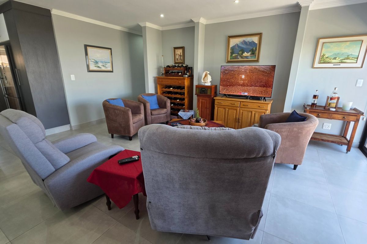 A spacious living room featuring neutral tiled flooring, recessed downlighting, and large sliding glass doors that provide access to the outdoor area.