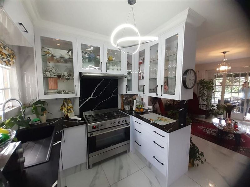 Modern kitchen featuring white cabinetry, glass-fronted display units, black marble-look countertops, and a gas stove with a matching splashback.