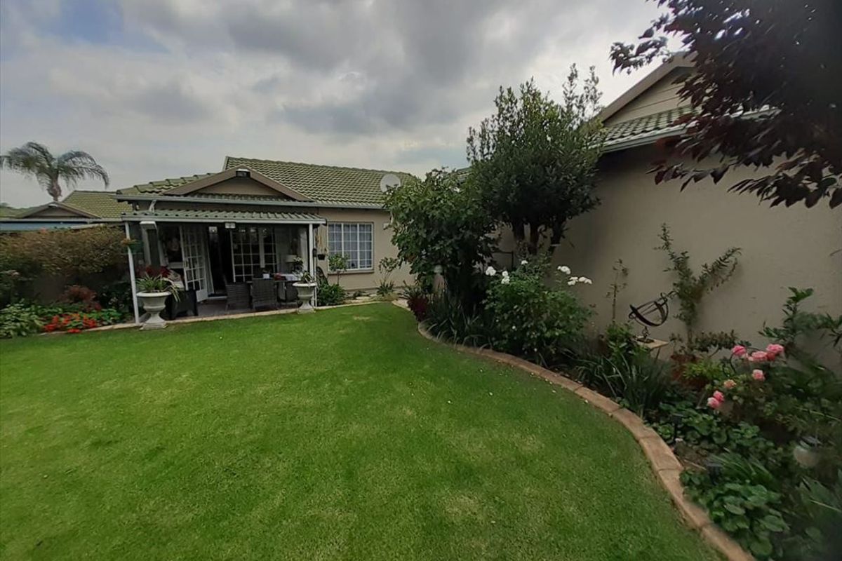A well-maintained rear garden featuring a lush lawn, established garden beds with brick edging, and a covered patio area attached to the townhouse.