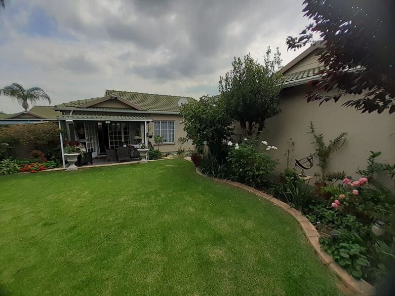 A well-maintained rear garden featuring a lush lawn, established garden beds with brick edging, and a covered patio area attached to the townhouse.
