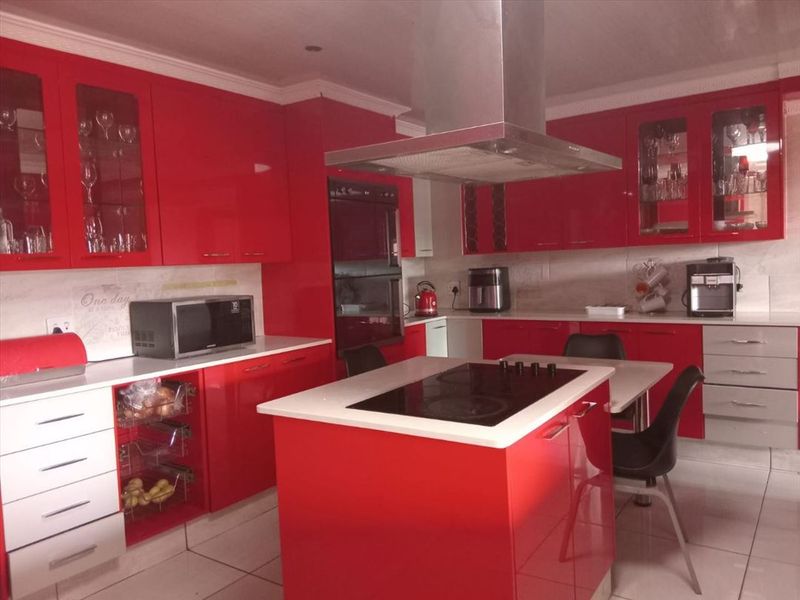 Modern kitchen featuring vibrant red high-gloss cabinetry, a central island with a built-in hob, stainless steel extractor fan, and tiled flooring.