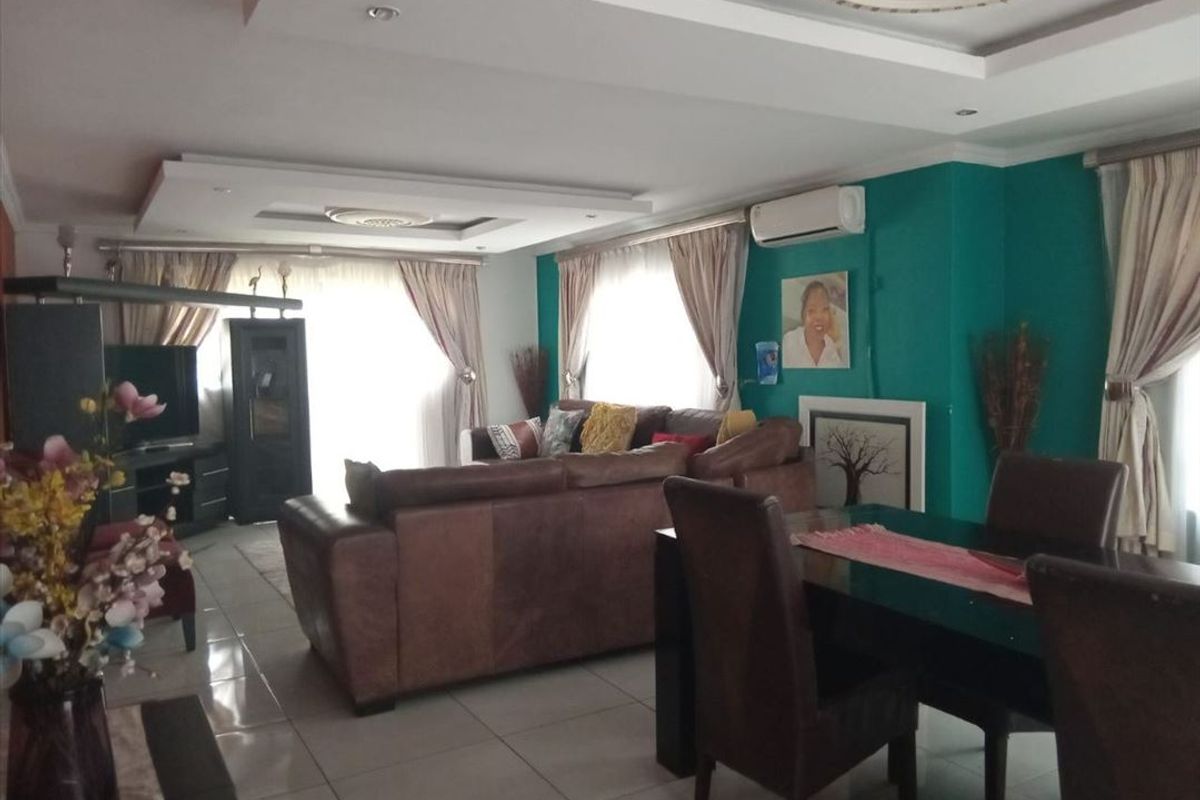 Spacious open-plan living and dining area featuring tiled flooring, recessed ceiling details with cove lighting, and a wall-mounted air conditioning unit.