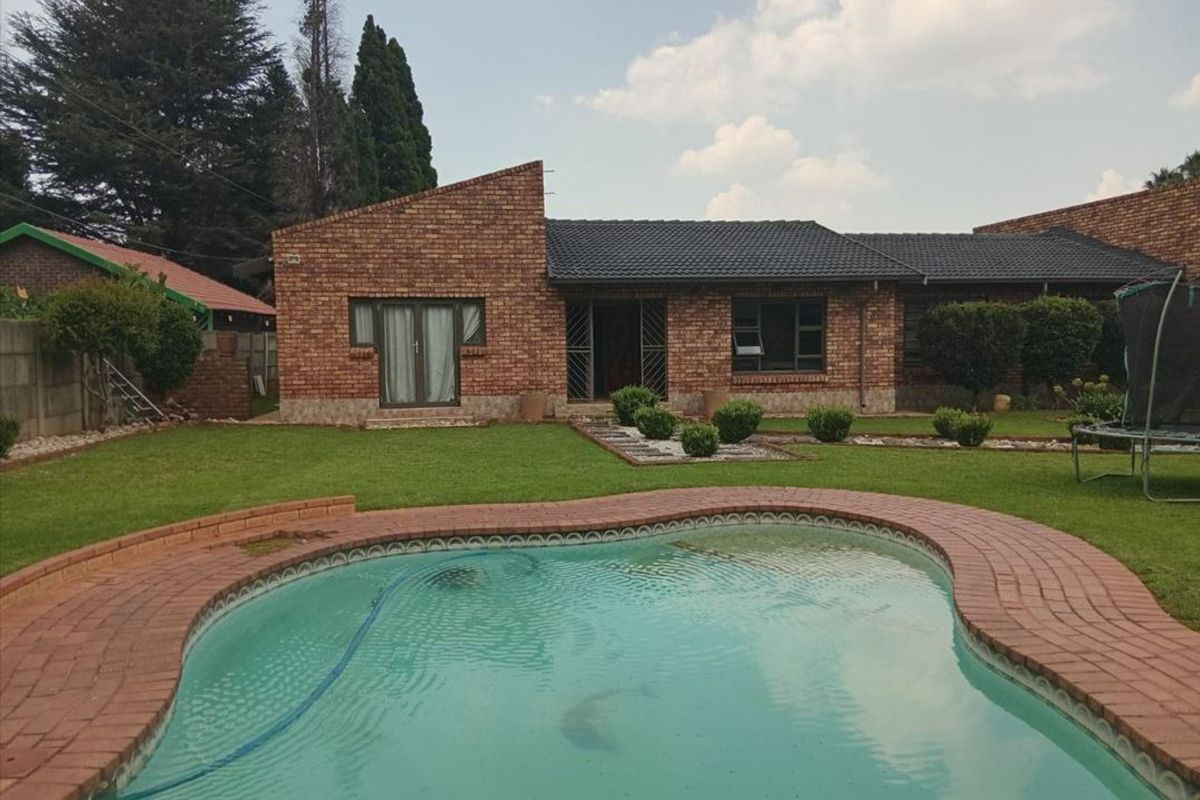 Rear view of a face brick house featuring a swimming pool, paved surround, and a well-maintained garden.