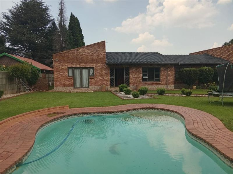 Rear view of a face brick house featuring a swimming pool, paved surround, and a well-maintained garden.