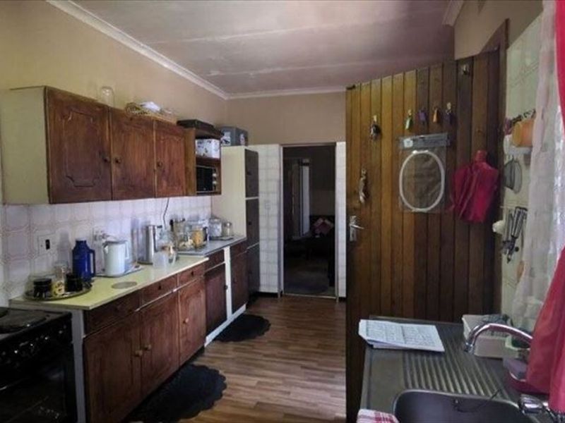 A functional kitchen featuring traditional wooden cabinetry, a built-in stove, and a stainless steel sink, offering a classic layout with potential for modernization.