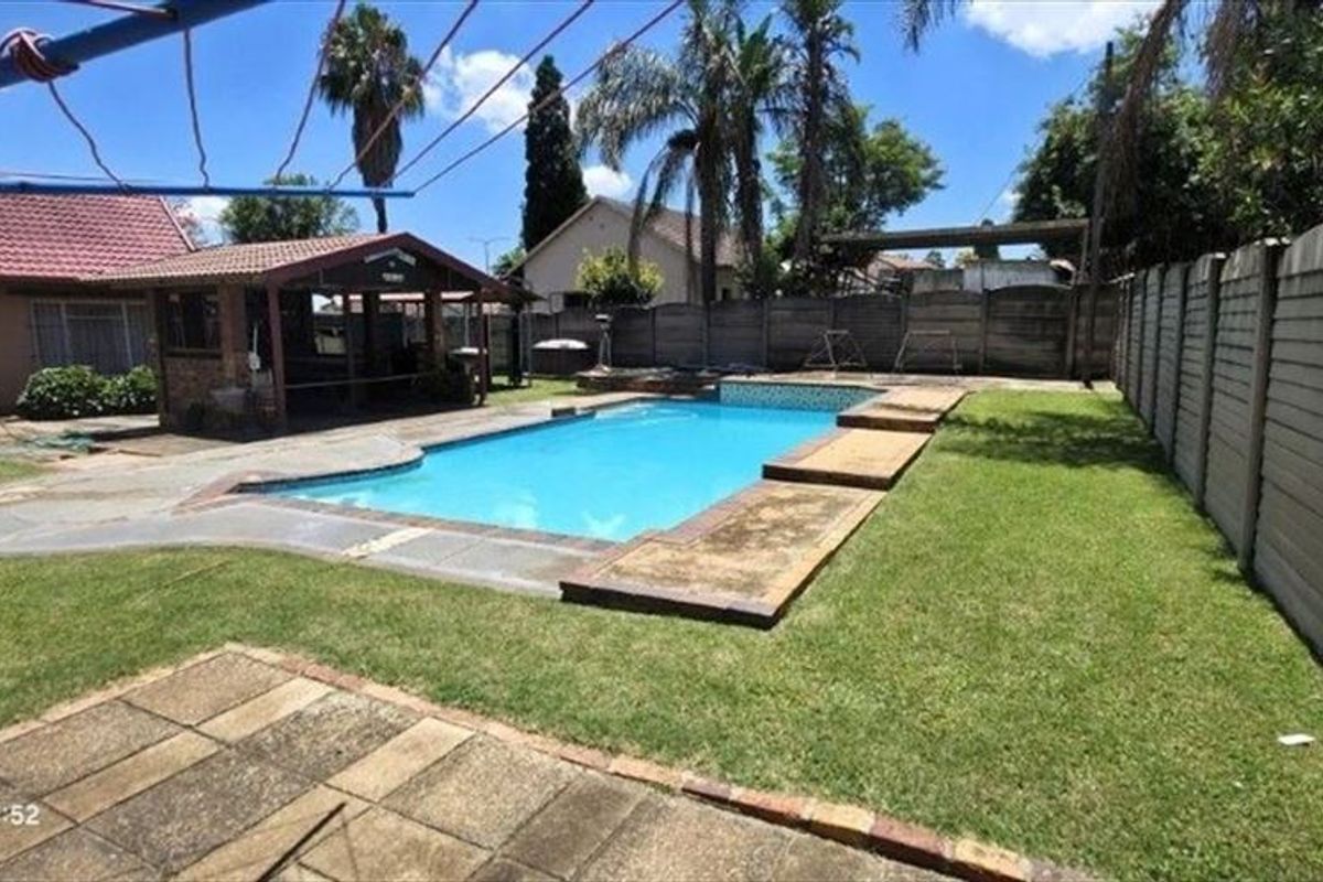 A private backyard featuring a swimming pool, a covered outdoor entertainment area, and a lawn enclosed by precast concrete boundary walls.