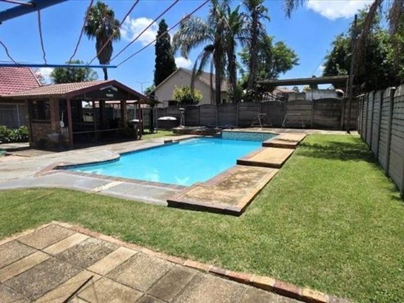 A private backyard featuring a swimming pool, a covered outdoor entertainment area, and a lawn enclosed by precast concrete boundary walls.