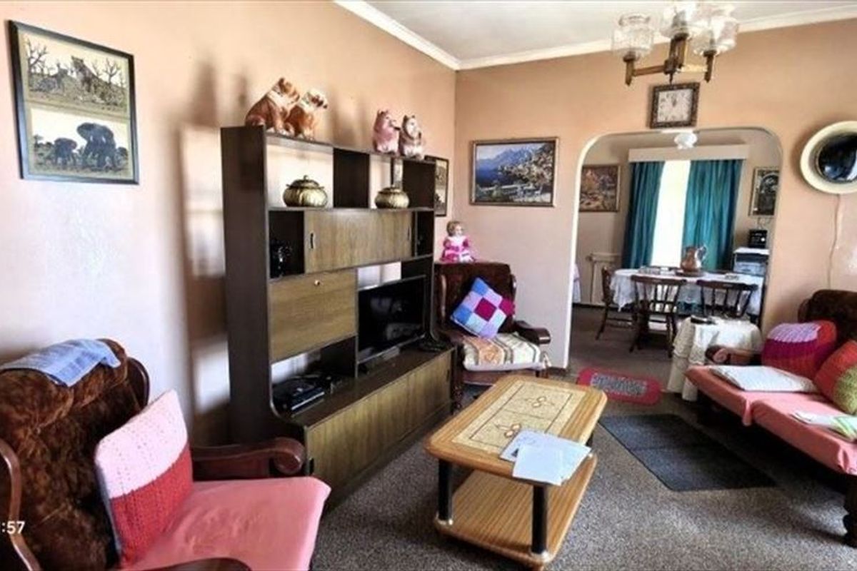 A traditional living room featuring an arched entryway leading to a dining area, with neutral wall finishes and carpeted flooring throughout.