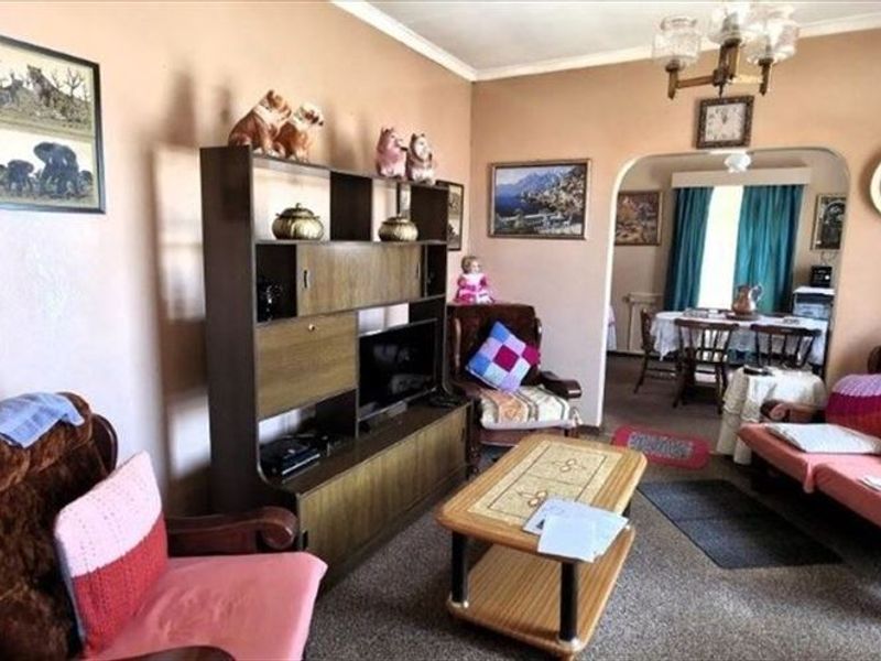 A traditional living room featuring an arched entryway leading to a dining area, with neutral wall finishes and carpeted flooring throughout.