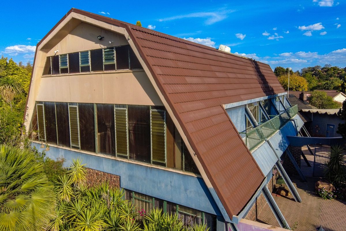 Aerial view of the rear elevation featuring a large tiled roof, extensive louvre window glazing, and a balcony overlooking the paved patio area.