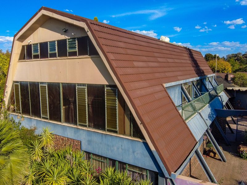 Aerial view of the rear elevation featuring a large tiled roof, extensive louvre window glazing, and a balcony overlooking the paved patio area.