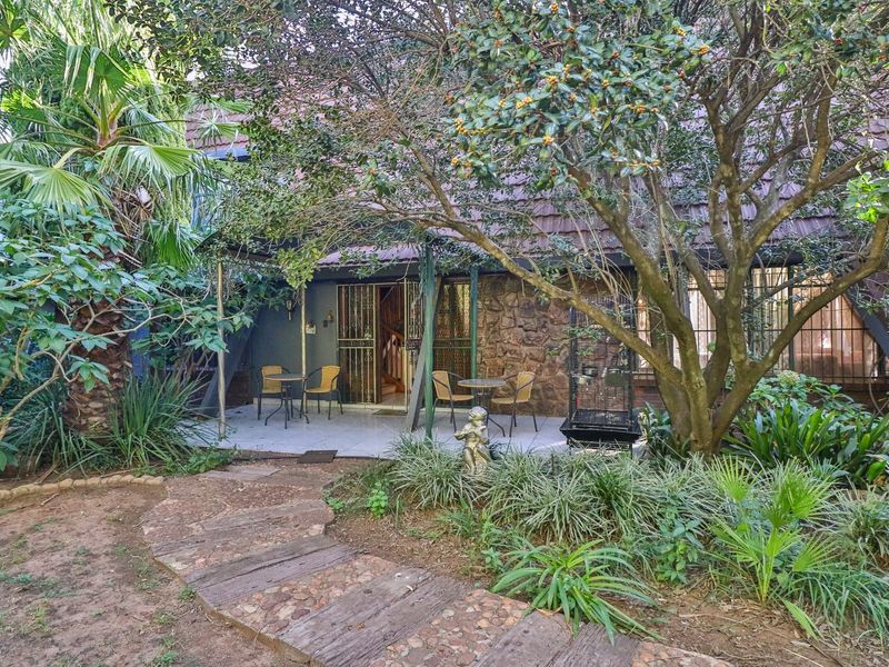 A covered patio area featuring stone cladding and tiled flooring, accessible via a garden path, offering a shaded outdoor space.