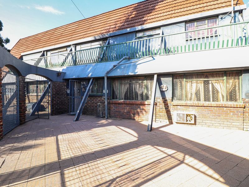 Rear exterior view of the property featuring a paved patio area, brick facade, and an upper-level balcony with metal railings.