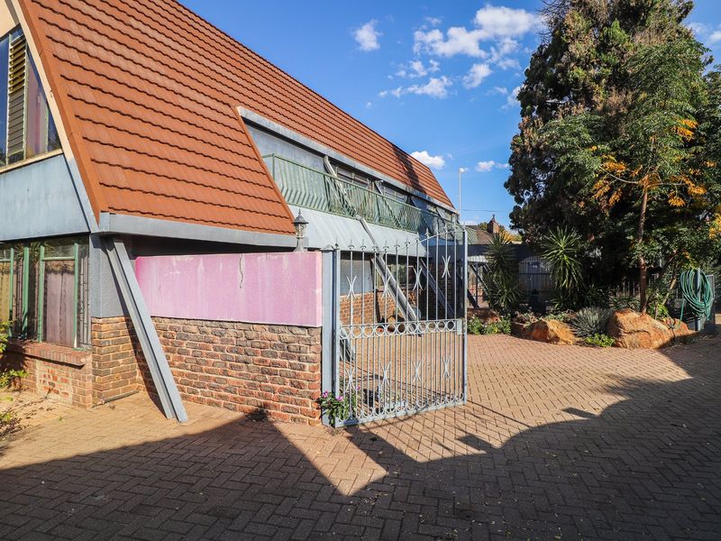 Rear exterior view of the property featuring a tiled roof, brick paved courtyard, and a secure metal gate with an upper-level balcony.