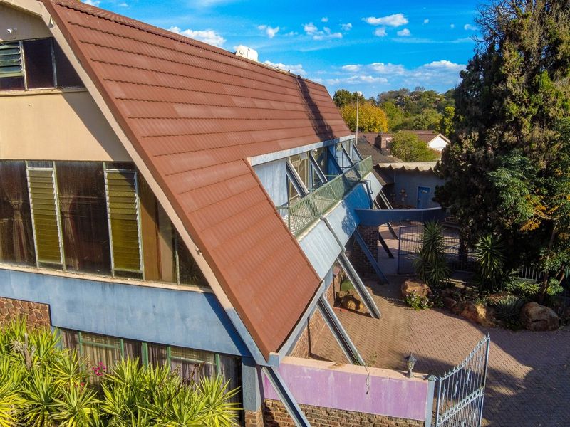 Aerial view of a unique A-frame style house featuring a tiled roof, balcony, and paved driveway entrance with security gate.