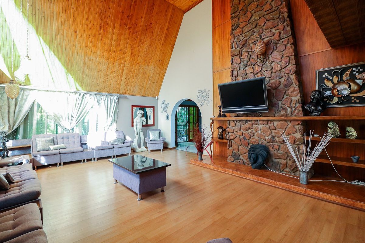 Spacious living room featuring a striking stone fireplace, high vaulted timber ceilings, and laminate flooring, creating a warm and character-filled atmosphere.