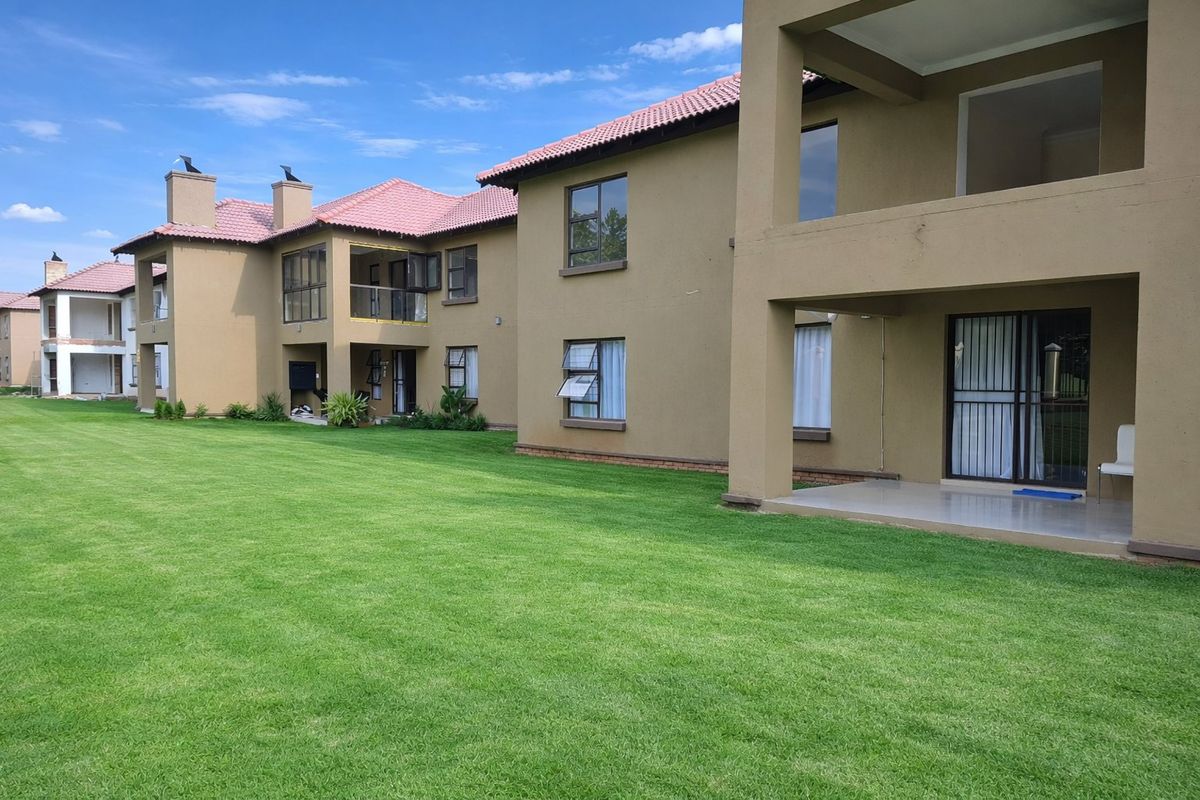 Rear view of a multi-story apartment complex featuring covered patios, tiled roofing, and well-maintained communal lawn areas.